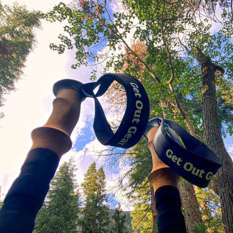 Hiker gripping Get Out Gear carbon fiber trekking poles with cork handles among tall trees